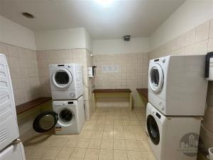 Prádelna s dlažbou a moderními pračkami, prostorná místnost vhodná pro více uživatelů, vybavená pro efektivní praní prádla.