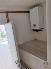 Malá technická místnost s moderním kotlem, dřevěné obložení a světlé stěny, ideální pro úsporné topení v rekonstruovaném domě.