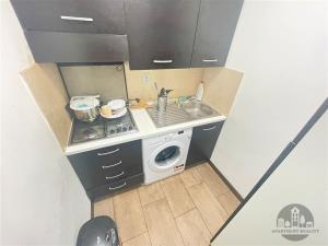 Malá kuchyň s tmavou dřevěnou skříňkou, parketovou podlahou a vestavěnou varnou deskou, ideální pro kompaktní bydlení.