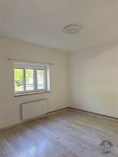 Světlý pokoj s laminátovou podlahou, velká okna a bílými stěnami. Okno poskytuje výhled do zahrady, ideální pro moderní bydlení.