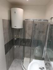 Koupelna s moderní sprchovým koutem a dlažbou, vybavená novým bojlerem a elegantními obklady, nabízí praktické využití prostoru.